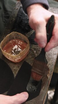 Vertical video. Footwear production. Shoe factory. Unrecognizable tailor hands smearing leather material using glue liquid with brush.