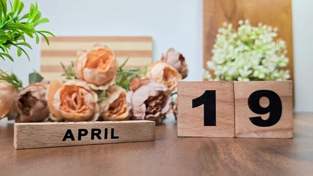 Hand placing wooden calendar blocks showing april 19 on a wooden table