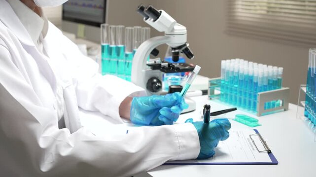 Focused scientist conducts chemistry research with microscope, blue liquid, test tube, writing on clipboard in laboratory