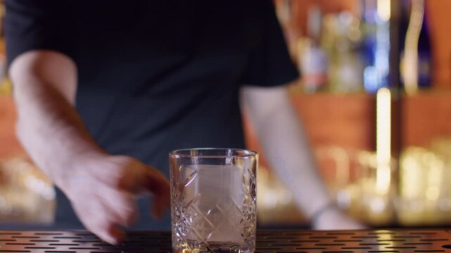 Hands serving drink. Cocktail making. Unrecognizable man bartender using ice cube into glass on bar counter for preparing alcohol beverage in pub.