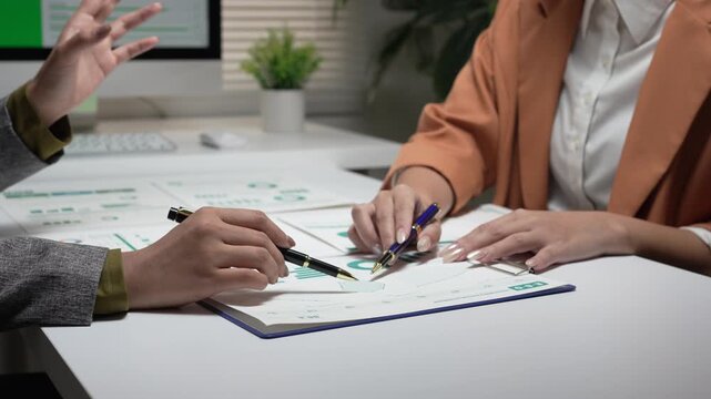 Focused business partner having collaborative discussion, pointing hand at financial document paper chart on office desk