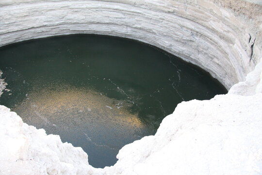 Darvaza sinkhole with emerald water in the Karakum Desert, Turkmenistan under clear blue sky. g.