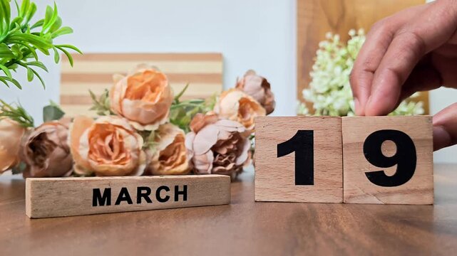 Hand placing wooden calendar blocks showing march 19 on a wooden table