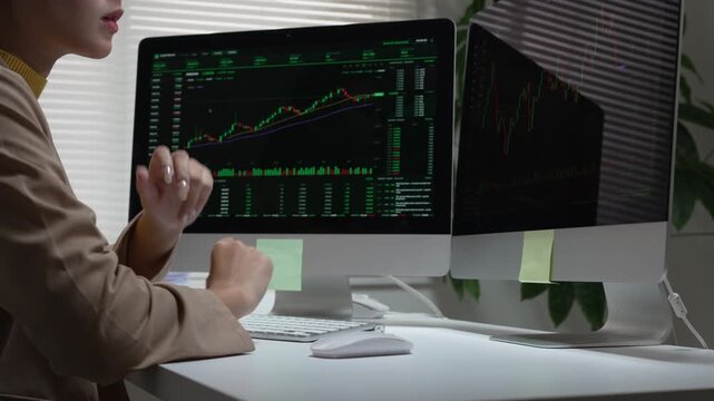 Focused thoughtful investor woman trader analyzing finance stock chart on computer monitor in dark office workspace