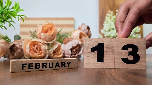 Hand placing wooden calendar blocks showing february 13 on a wooden table