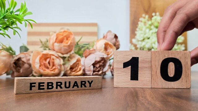 Hand placing wooden calendar blocks showing february 10 on a wooden table