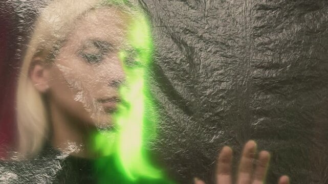 Quarantine isolation. Self measures. Conceptual art. Stay safe. Woman touching transparent plastic film staying behind on red green background defocused copy space.