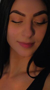 Vertical video. Glowing skin. Confident model. Girl caressing face touching long healthy hair. Attractive radiant charm female posing in night light.
