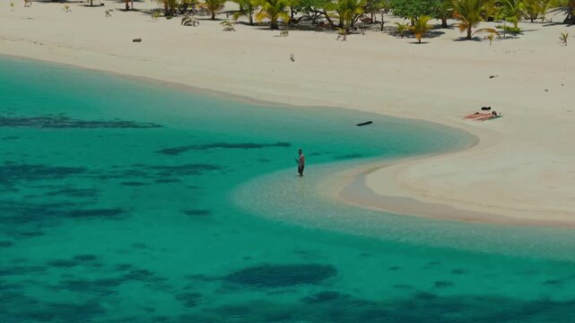 Aerial tracking orbit of a man standing in crystal clear water at Patawan Island, Balabac, Philippines. Cinematic 360 drone shot of person in shallow tropical turquoise sea.
