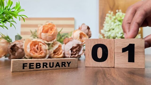 Hand placing wooden calendar blocks showing february 1 on a wooden table