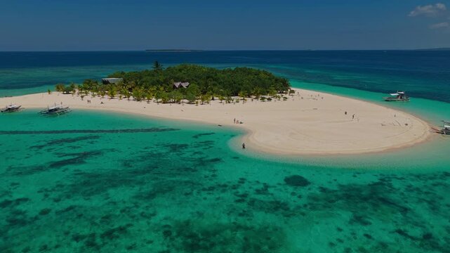 Aerial drone descent to land at Patawan Island tracking a man standing in crystal clear water, Balabac, Philippines. Inbound landing approach over shallow turquoise sea towards tropical beach.