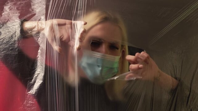 Stop problem. Plastic recycling. Pure air. Woman tearing apart transparent polyethylene film putting off protective mask making deep breath on red green background defocused.