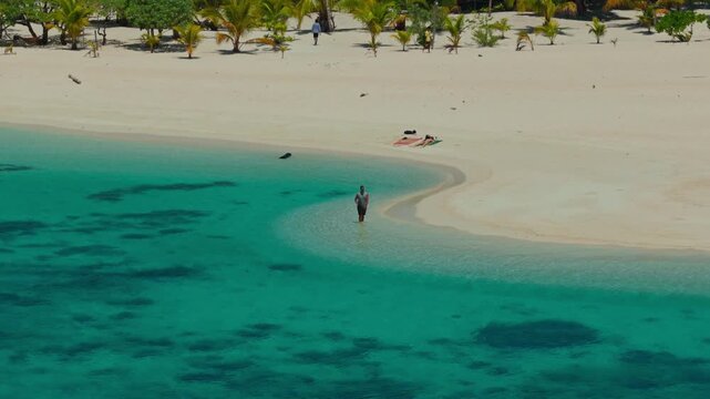 Man walking through crystal clear shallow turquoise ocean water on Patawan Island, Balabac, Philippines. Slow motion tracking shot of feet walking on tropical white sand beach.