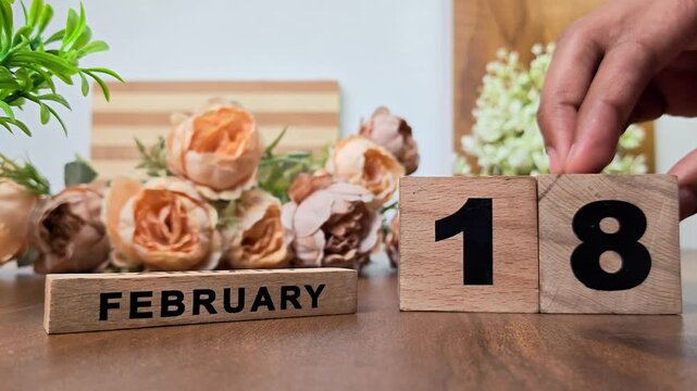 Hand placing wooden calendar blocks showing february 18 on a wooden table