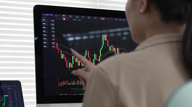 Focused female investor analyzing financial stock market chart on computer screen inside modern professional office environment