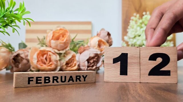 Hand placing wooden calendar blocks showing february 12 on a wooden table