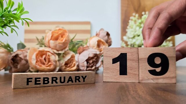 Hand placing wooden calendar blocks showing february 19 on a wooden table