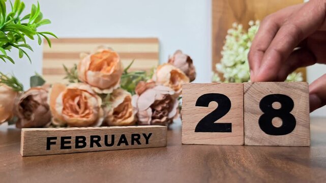 Hand placing wooden calendar blocks showing february 28 on a wooden table