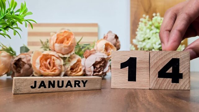 Hand placing wooden calendar blocks showing january 14 on a wooden table
