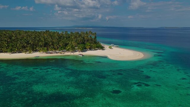 Aerial drone flight flying from open sea towards Tangkahan Island, Balabac, Palawan, Philippines. Inbound tracking shot over deep ocean approaching tropical hook sandbar.