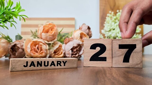 Hand placing wooden calendar blocks showing january 27 on a wooden table