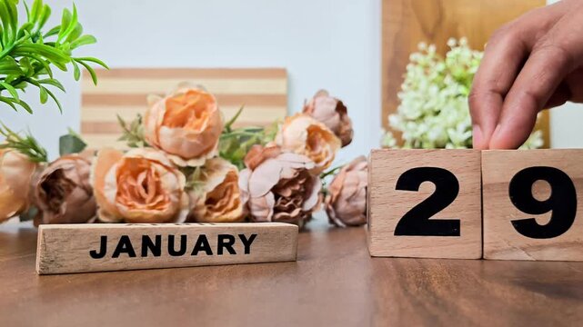 Hand placing wooden calendar blocks showing january 29 on a wooden table