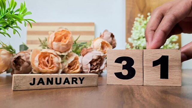 Hand placing wooden calendar blocks showing january 31 on a wooden table