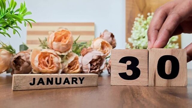 Hand placing wooden calendar blocks showing january 30 on a wooden table