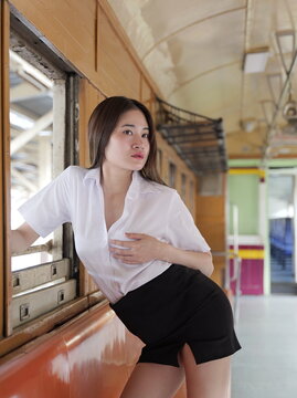 A young Asian woman in a white student uniform shirt and black skirt poses inside an old train car