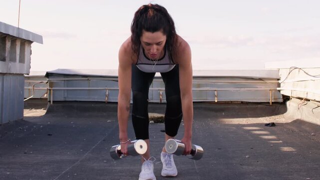Weight training. Outdoor strength. Active female athlete enjoying fitness practice performing physical healthy exercise on rooftop.