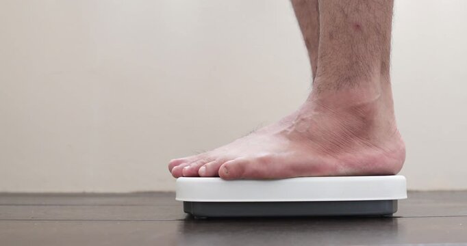 Close up of male bare feet stepping on a digital weight scale on wooden floor, health, diet and weight loss concept.