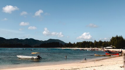 Idyllic tropical beach with anchored boats, clear blue water, sandy shore, and lush green hills under a bright sky © suciramadhani
