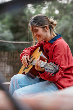 Woman playing acoustic guitar, smiling with joy outdoors