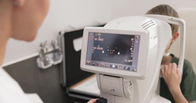 Close up modern digital ophthalmic microscope monitor displaying eye structure with diagnostic data and doctor examining little patient during regular child vision health checkup in children clinic