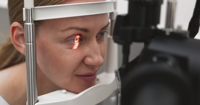 Close up young adult woman patient completing computerized eye screening procedure on optical testing machine passing vision diagnostics on professional ophthalmic equipment during routine examination