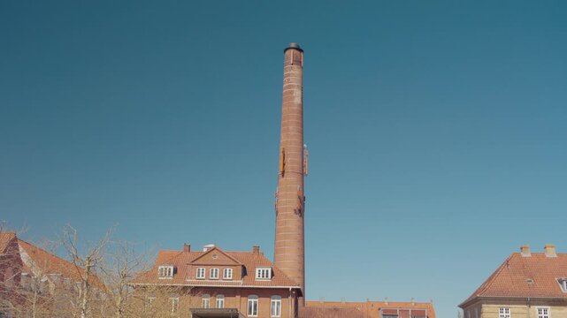 A tall old brick industrial chimney rises against a clear blue sky in Haderslev, southern Denmark.