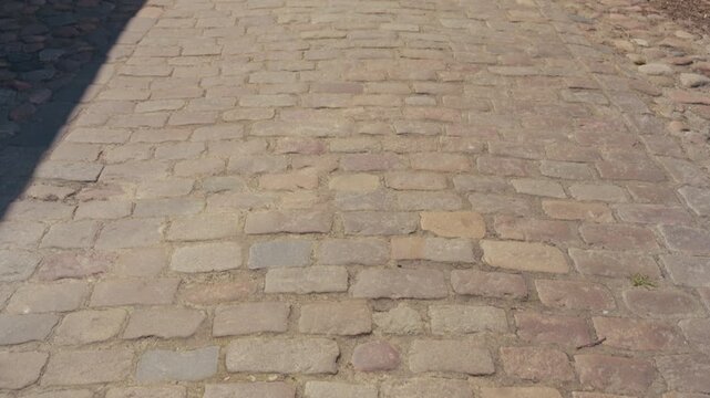 Close view of an old cobblestone pavement forming a textured pattern of weathered stones in warm daylight.