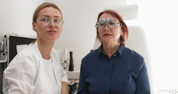 Eye clinic doctor changing lenses in trial frame system on face of middle aged woman patient discussing visual comfort and clarity during eyesight exam for correct selection of prescription glasses
