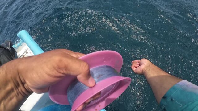 POV shot of a traditional fisherman manually pulling a line to catch fish from a small boat, capturing the raw technique of artisanal fishing.