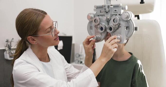 Pediatric ophthalmologist providing phoropter testing for eye screening of young patient evaluating eyesight quality and vision sharpness representing caring and qualified children medical service