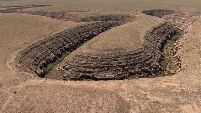 4K UHD drone flight showcasing a massive winding dry river canyon in the Arizona desert. A tiny black car on a remote dirt trail highlights the epic scale of this rugged adventure travel destination.