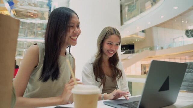 Two cheerful asian women videocalling on laptop