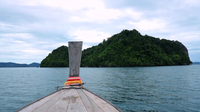 boat approaching rocky island in ocean under cloudy sky with serene and adventurous mood, front view from wooden boat, travel and adventure context, blue and green tones, clean and natural.