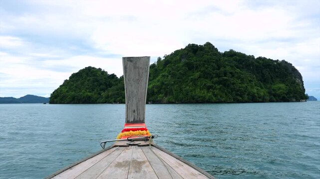 peaceful longtail boat approaching lush island in serene ocean setting from front perspective. travel and vacation adventure in natural blue and green environment.
