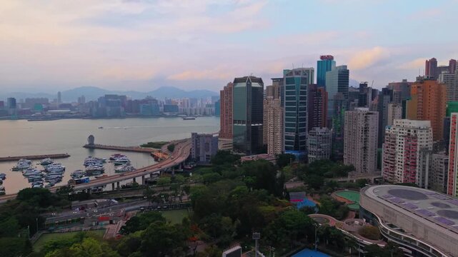 Aerial view of vibrant urban skyline with harbor and busy highway traffic against a backdrop of mountains at dusk.