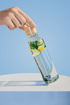 Hand holding glass bottle filled with refreshing detox water on blue background