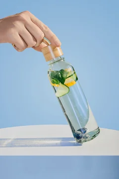 Hand holding glass bottle filled with refreshing detox water on blue background