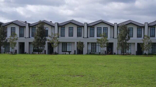 Modern uniform townhouses or contemporary terrace housing estate facing a green park with a kid riding a bike along the front pathway, Melbourne outer suburbs, Victoria, Australia.