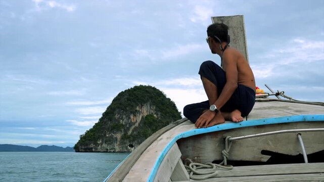 man sitting on a wooden boat, relaxing and contemplating ocean scenery with islands in the background, side view of a leisurely vacation moment in a serene setting.
