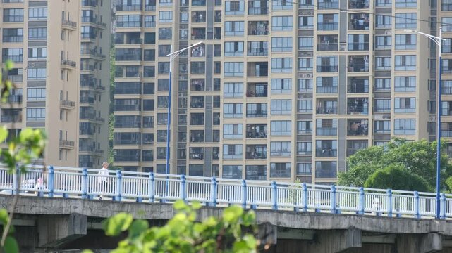 Person walking across a bridge with dense highrise residential towers in background in Guangxi, China. Urban housing oversupply and population density. Real estate, city planning, Chinese urban growth